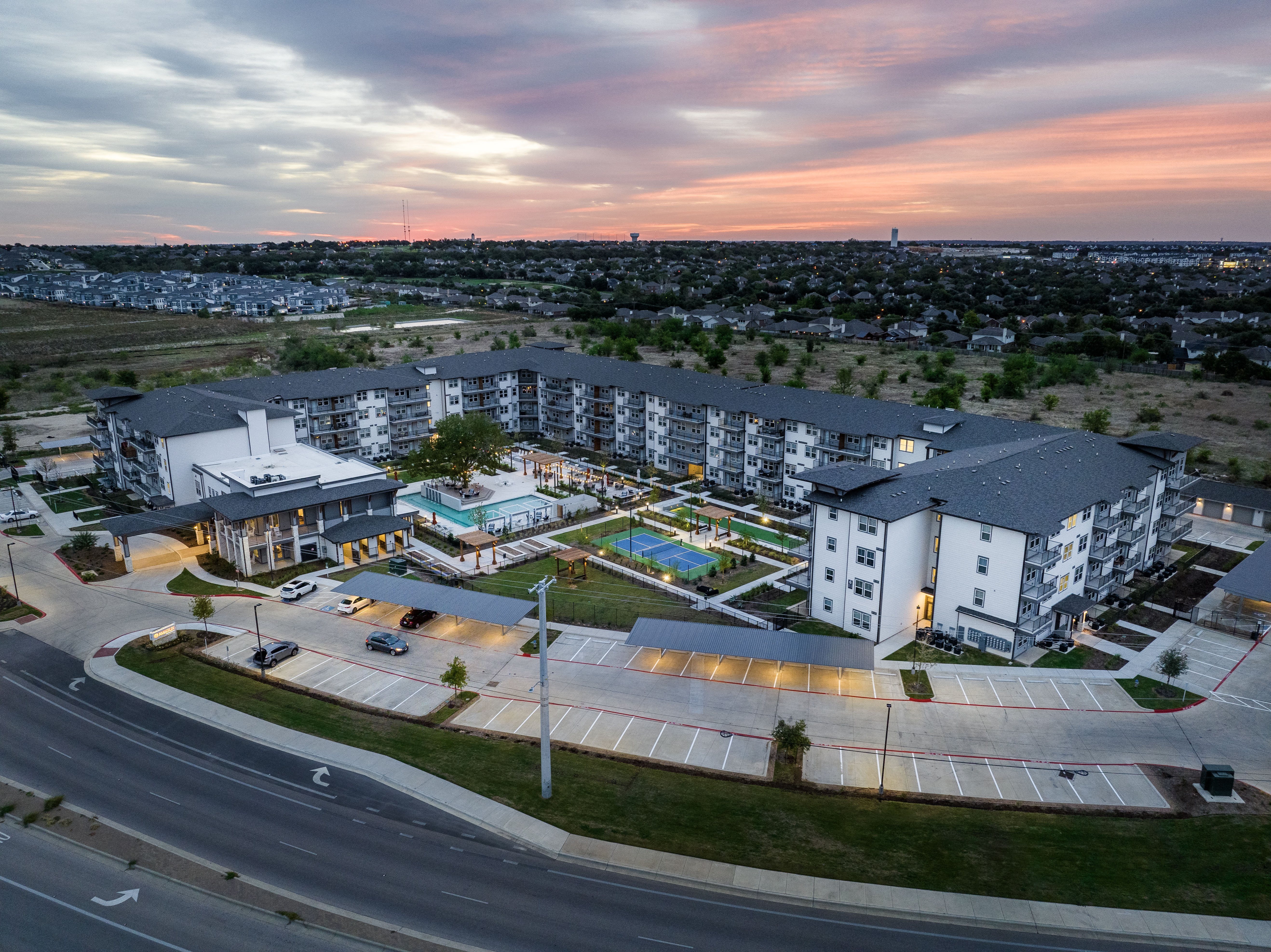 an aerial, street-view of an apartment building, courtyard, resort-style pool, and lawn at a senior apartment community